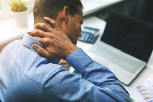 office syndrome – man suffering from neck and back pain while working with computer