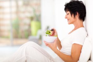 elegant middle aged woman sitting on bed and eating salad